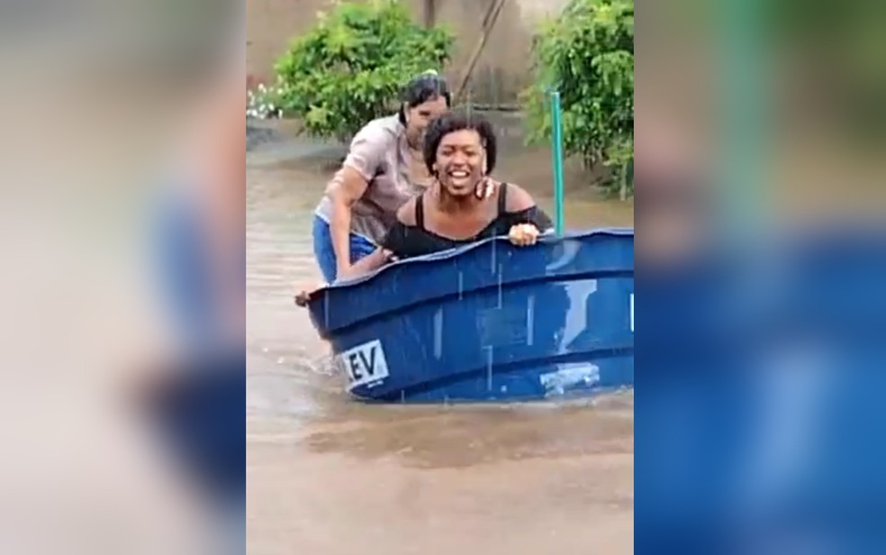 Moradora usa caixa d'água como barco em rua alagada de Goiânia