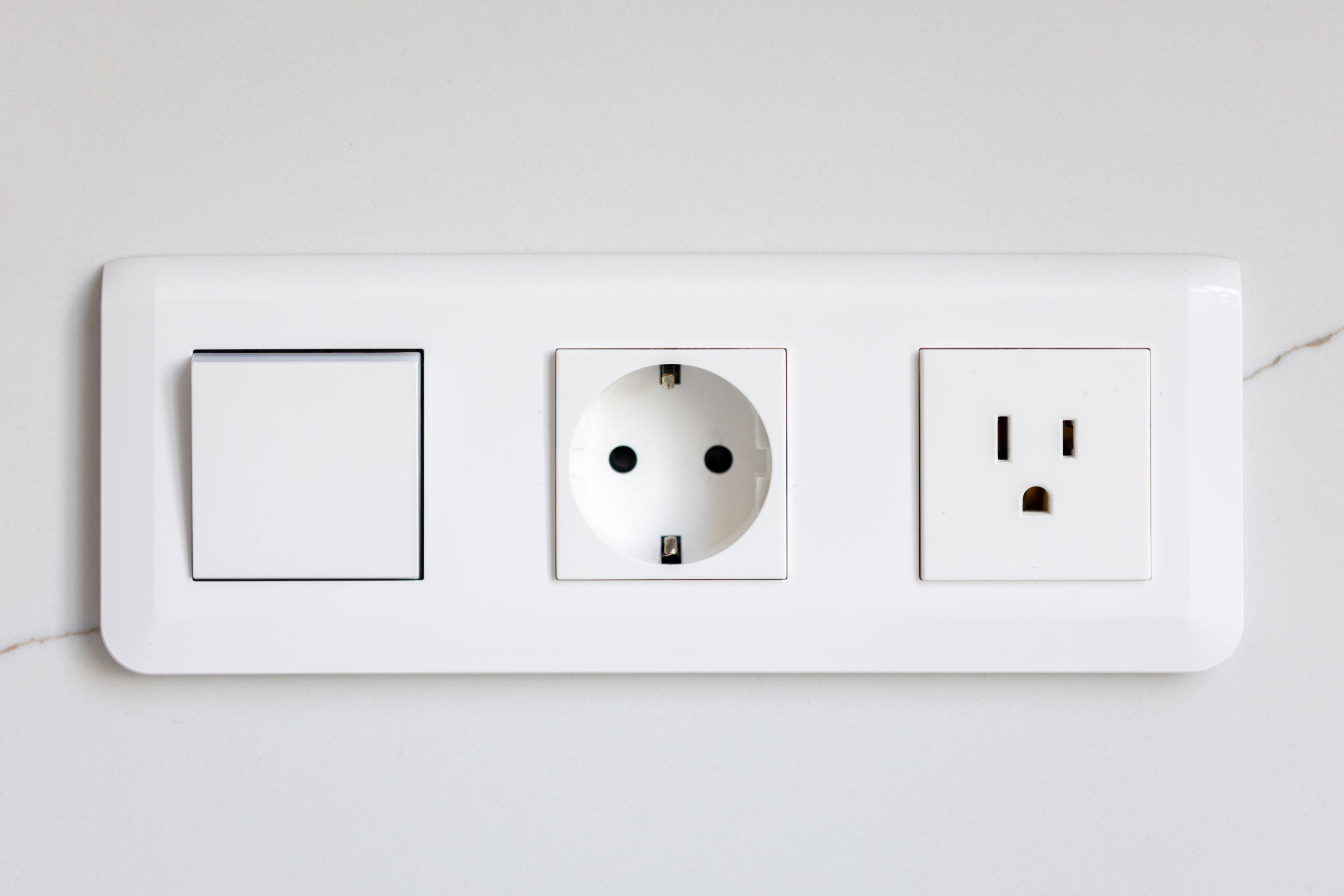 White wall block with a switch and two sockets of different standards on a smooth surface. A clean electrical installation with modern minimalist style.