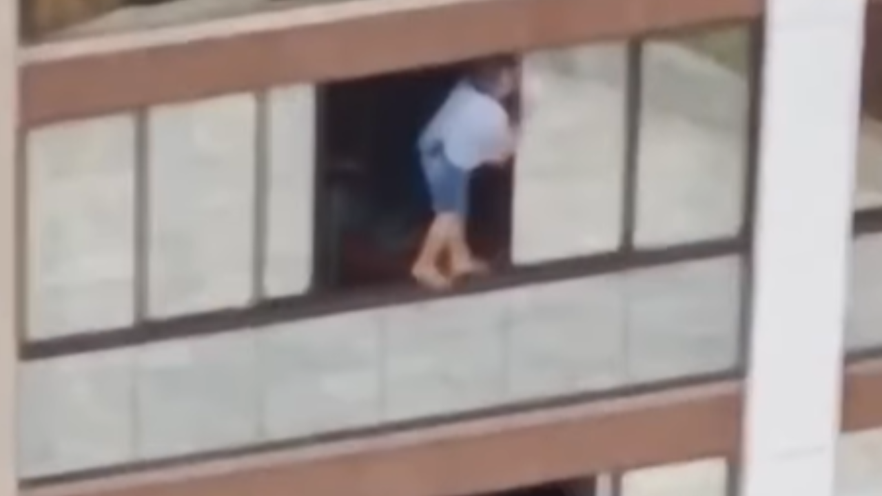 Mulher se arrisca em parapeito para limpar janela em prédio